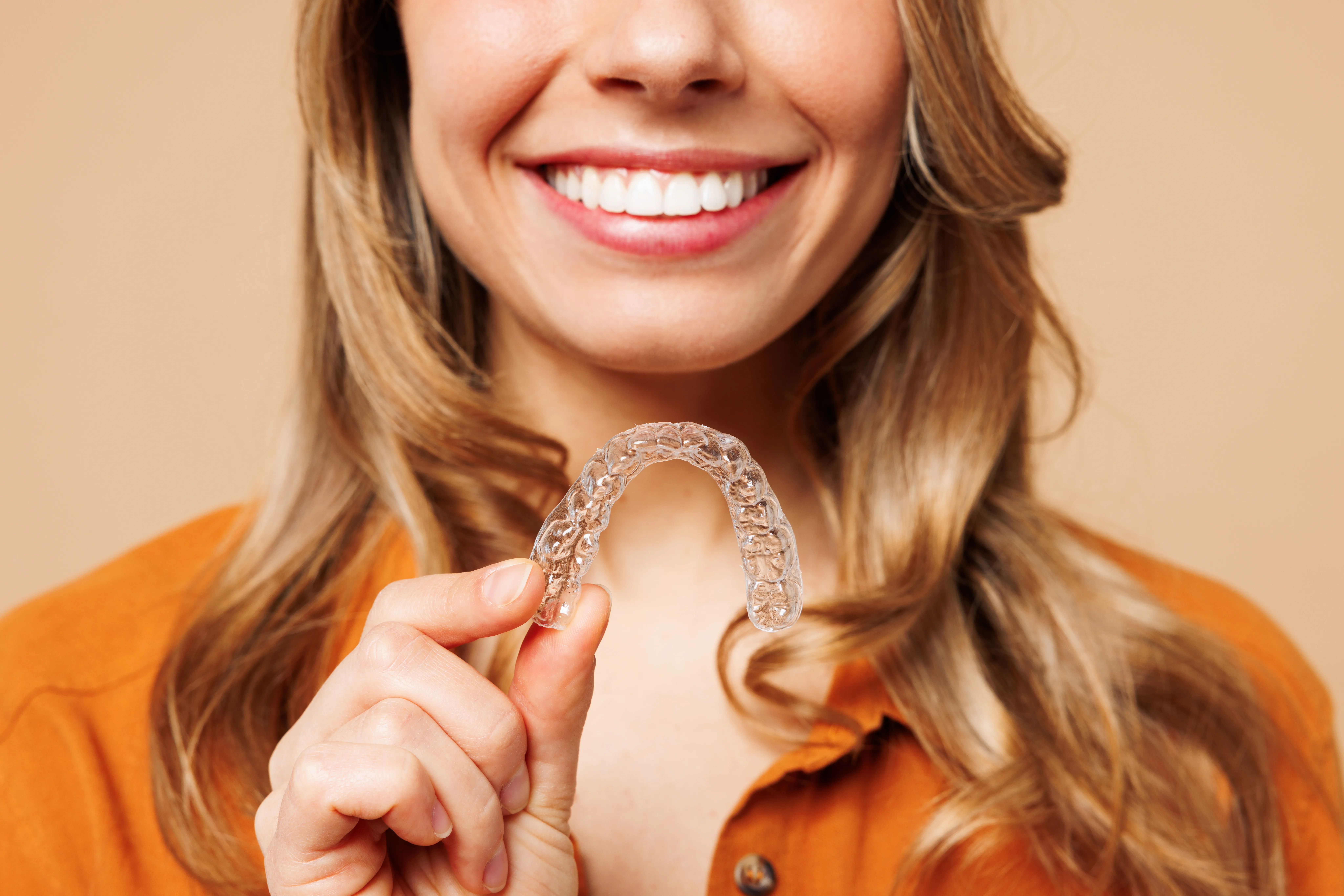 Smiling woman holding up a clear aligner tray