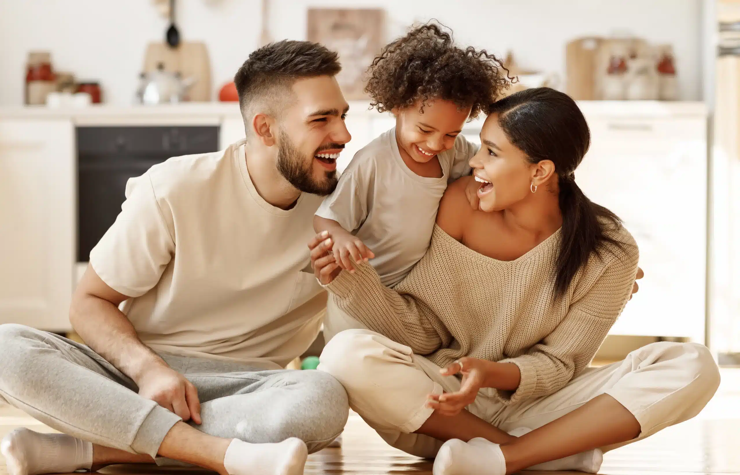 A diverse, laughing family sits on the floor, embodying Our Core Values at Des Peres Dentistry