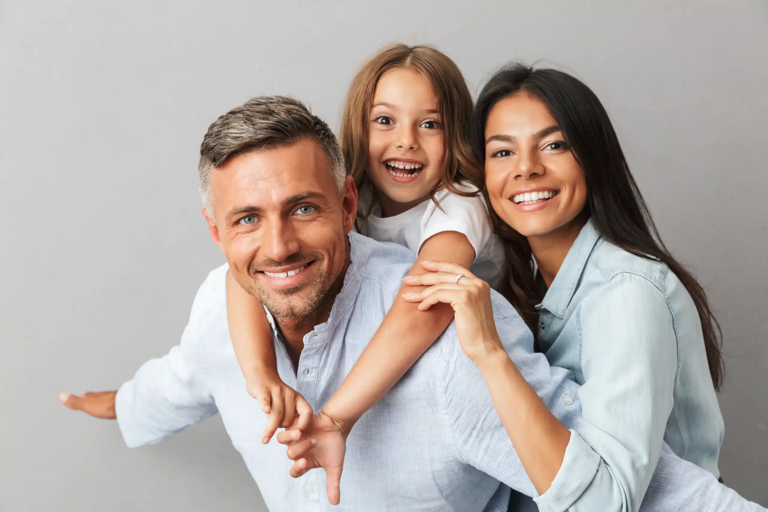 A happy family, with a father giving a piggyback ride, all smiling, thanks to Des Peres Dentistry